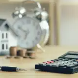 Calculator on table in front of house and alarm clock