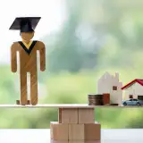 Person with graduation cap on a scale, balancing with a house
