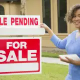 real estate agent standing next to a for sale sign with a rider reading sale pending