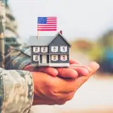 military service member holding a small home with an american flag