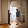 A real estate agent explains FHA repair escrow details to a couple in a spacious, well-lit empty room.