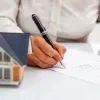 Homeowner signing paperwork next to a small house sitting on desk