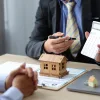 Person holding a calculator next to the model of a house.