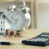 Calculator on table in front of house and alarm clock