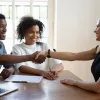 a couple with a contract in front of them shaking hands with their real estate agent