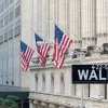 Photo of building exterior with hanging American flags and a wall street street sign in front.