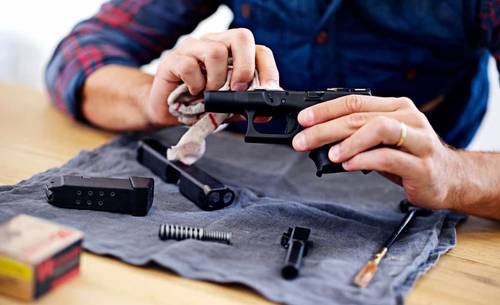 A guy cleaning his glock pistol and cleaning tools on the table.