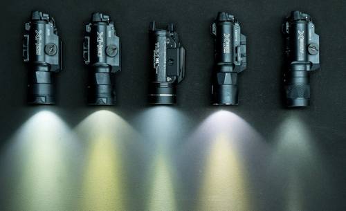 A set of 5 tactical flashlights for handguns on the table with light on.