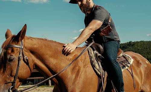 a guy with a shouler rig and cowboy look on a horse