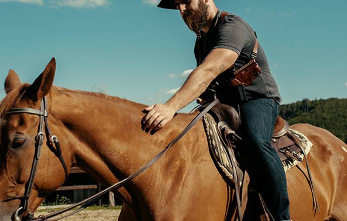 a guy with a shouler rig and cowboy look on a horse