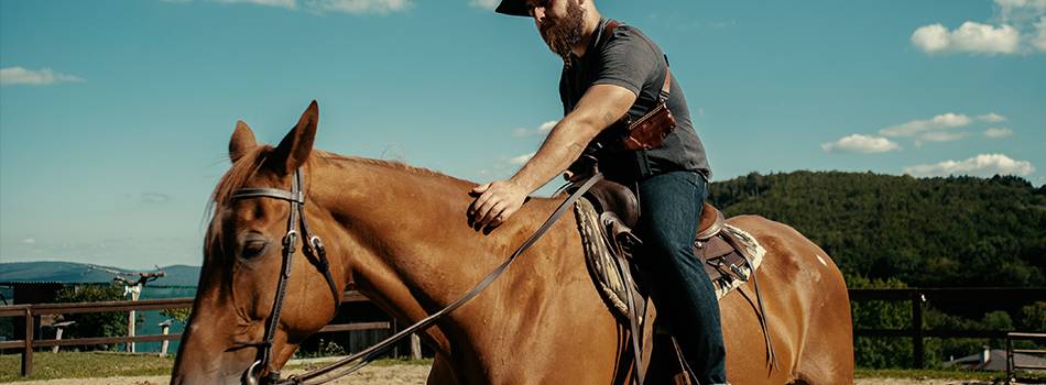 a guy with a shouler rig and cowboy look on a horse