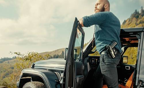 A guy with a fancy beard standing on the rim of his car looking into distance seeing his miserable future