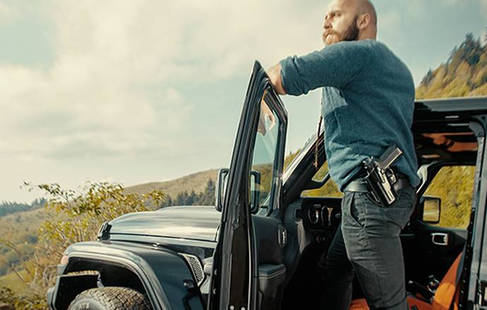 A guy with a fancy beard standing on the rim of his car looking into distance seeing his miserable future