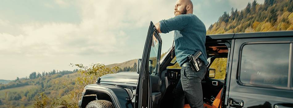 A guy with a fancy beard standing on the rim of his car looking into distance seeing his miserable future