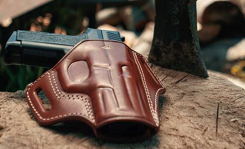 An OWB holster lying on a tree trunk with an axe next to it