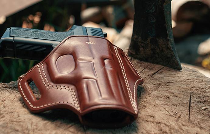 An OWB holster lying on a tree trunk with an axe next to it