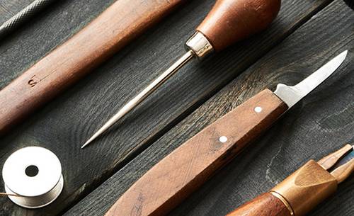 Close up shot of leather working tools lying on a black wooden table.