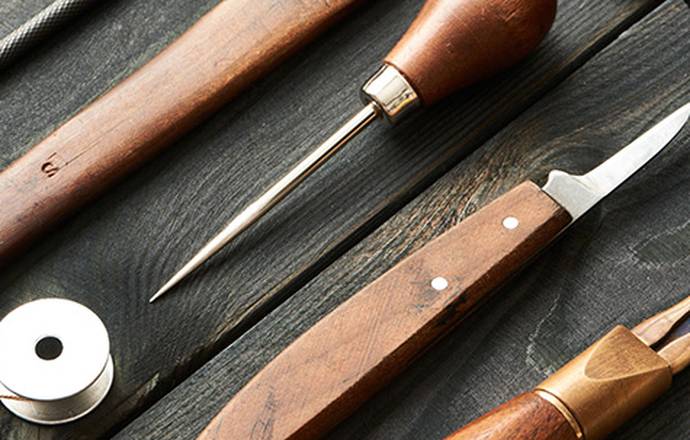 Close up shot of leather working tools lying on a black wooden table.