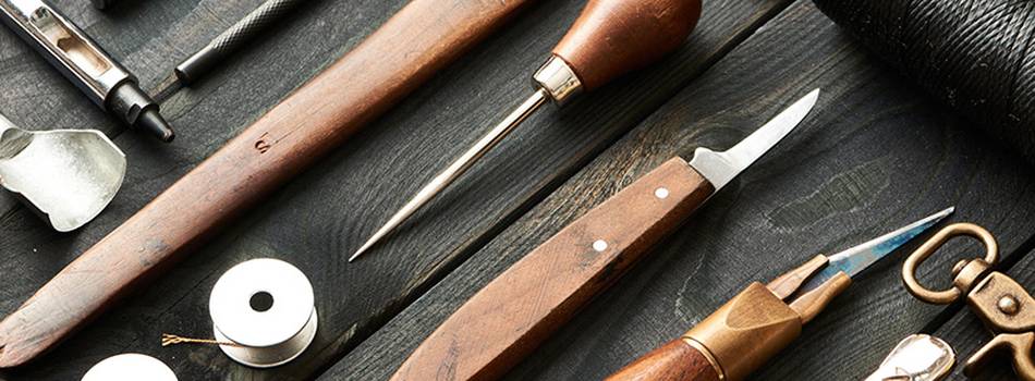 Close up shot of leather working tools lying on a black wooden table.