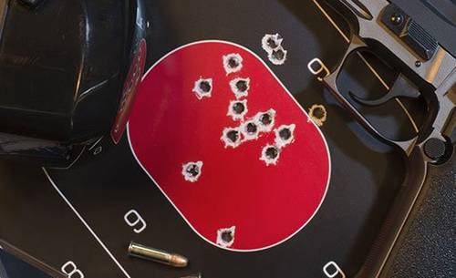 A pistol lying next to a shooting target full of holes, ear muffles and box of pistol ammo.