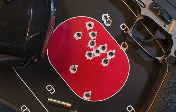 A pistol lying next to a shooting target full of holes, ear muffles and box of pistol ammo.