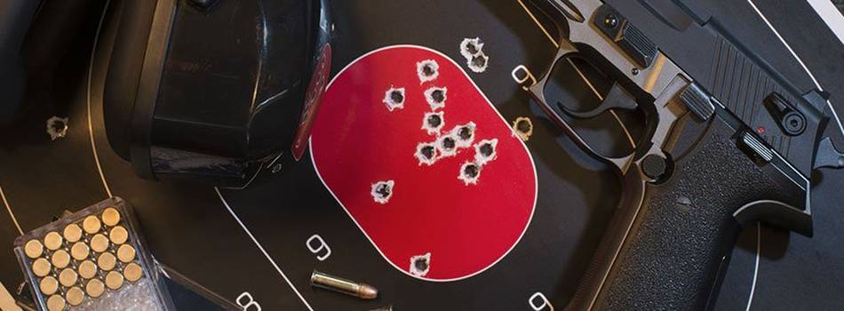 A pistol lying next to a shooting target full of holes, ear muffles and box of pistol ammo.