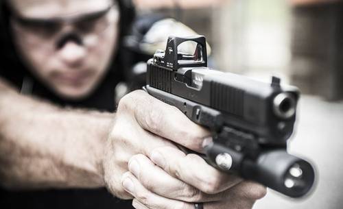 A guy aiming with his pistol equipped with a red dot sight