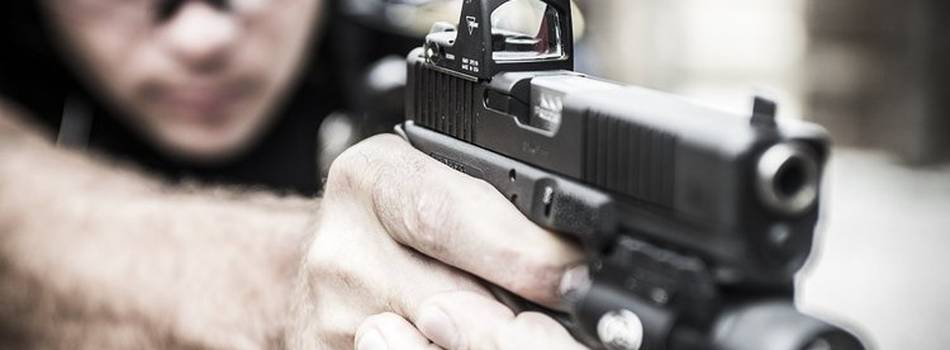 A guy aiming with his pistol equipped with a red dot sight