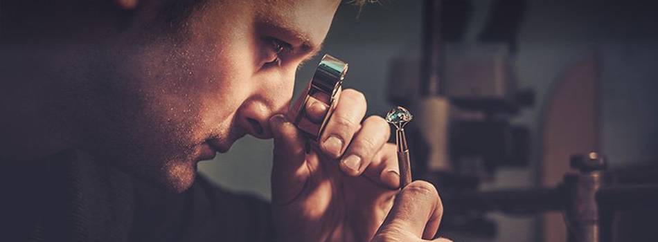 Jewelry expert checking a diamond through a magnifying glass in his workshop.