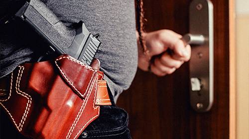 A guy with a chest holster tucked under a red checkered shirt looking into distance