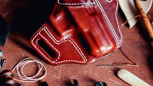 A leather OWB holster lying on a crafting desk with a lot of crafting tools around it