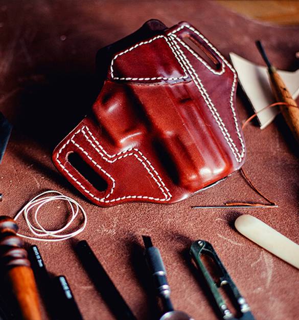 A leather OWB holster lying on a crafting desk with a lot of crafting tools around it