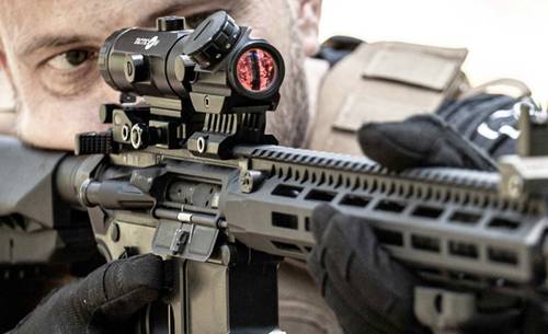 A soldier aiming through his AR-15 rifle red dot sight