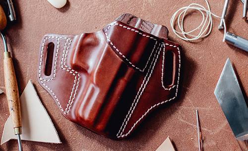 A leather holster in mahogany color for semi-automatic pistol with a bunch of crafting tools around it