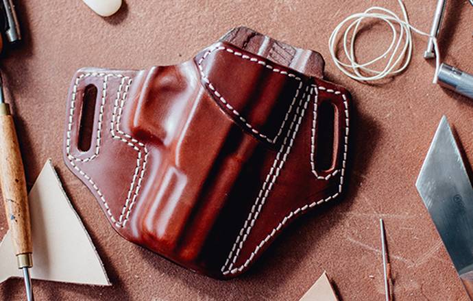 A leather holster in mahogany color for semi-automatic pistol with a bunch of crafting tools around it