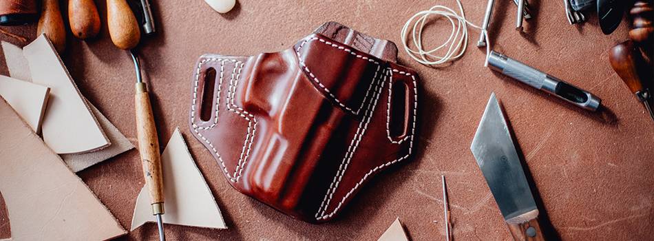 A leather holster in mahogany color for semi-automatic pistol with a bunch of crafting tools around it