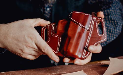 A craftsman showcasing a beautiful mahogany leather holster he's just finished.