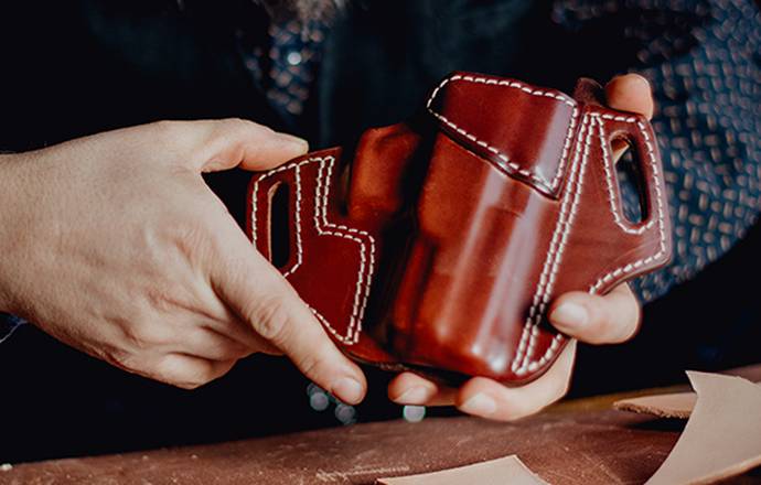 A craftsman showcasing a beautiful mahogany leather holster he's just finished.