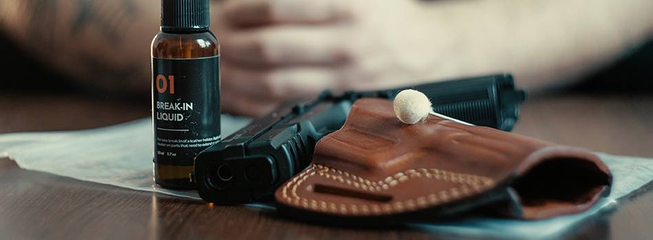 A leather OWB holster and a break-in liquid vial on a table, plastic bag underneath, a guy's arms in the background