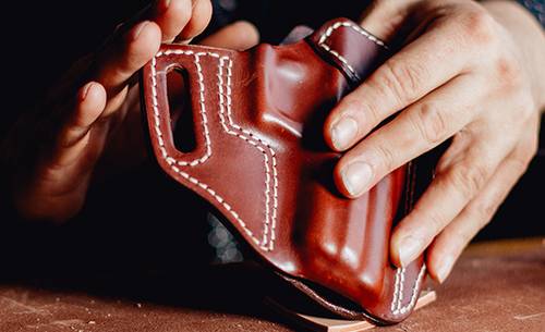 A leather craftsman holding a freshly crafted Kimber R7 Mako leather holster