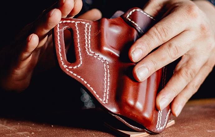 A leather craftsman holding a freshly crafted Kimber R7 Mako leather holster