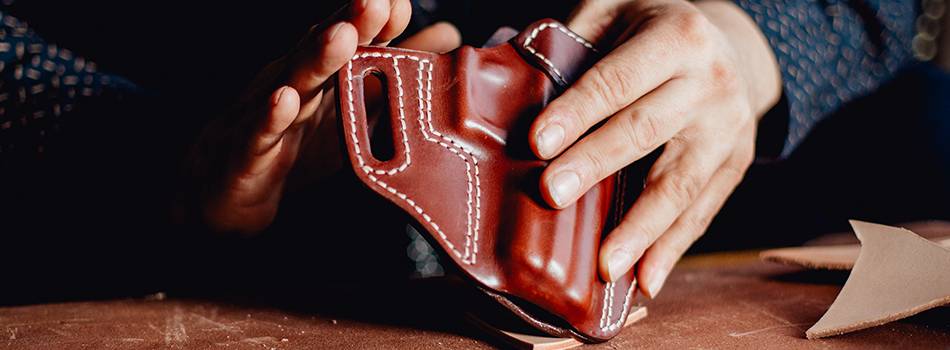 A leather craftsman holding a freshly crafted Kimber R7 Mako leather holster