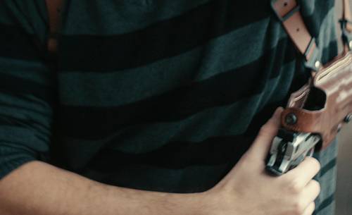 A guy drawing his 1911 pistol from a leather shoulder holster for horizontal carry