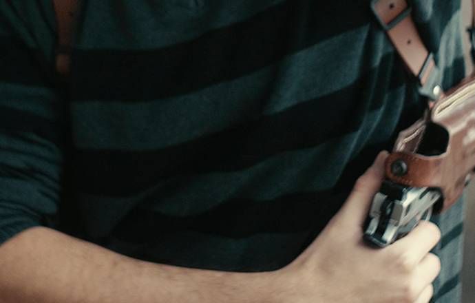 A guy drawing his 1911 pistol from a leather shoulder holster for horizontal carry