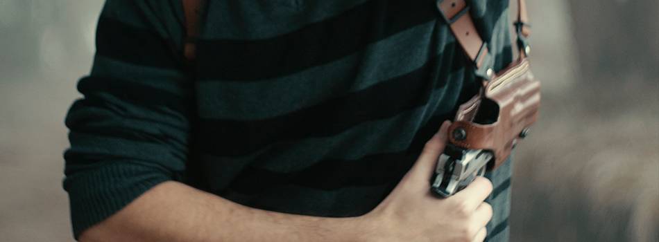 A guy drawing his 1911 pistol from a leather shoulder holster for horizontal carry