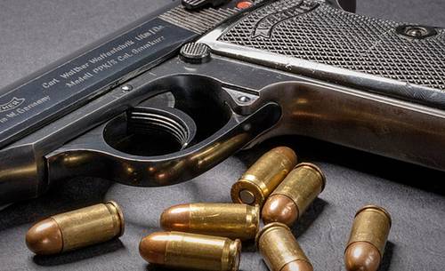 Walther PPK pistol on a desk with bullets dispersed around it