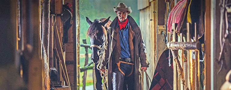 A cowboy leading his horse in a stable