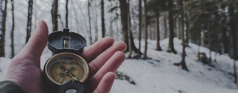 A hand holding a compass in a winter forest