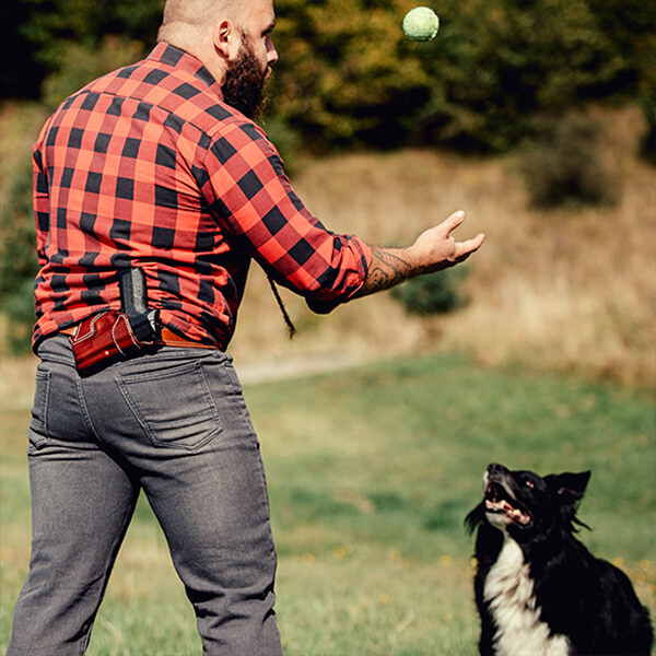 a guy with a leather small of the back holster playing fetch with his dog and a tennis ball