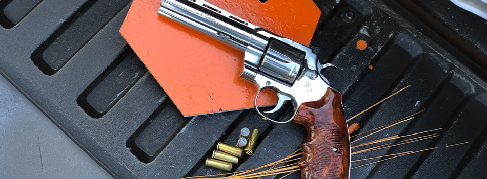 Colt Python revolver with ammunition and shooting targets at an outdoor range.